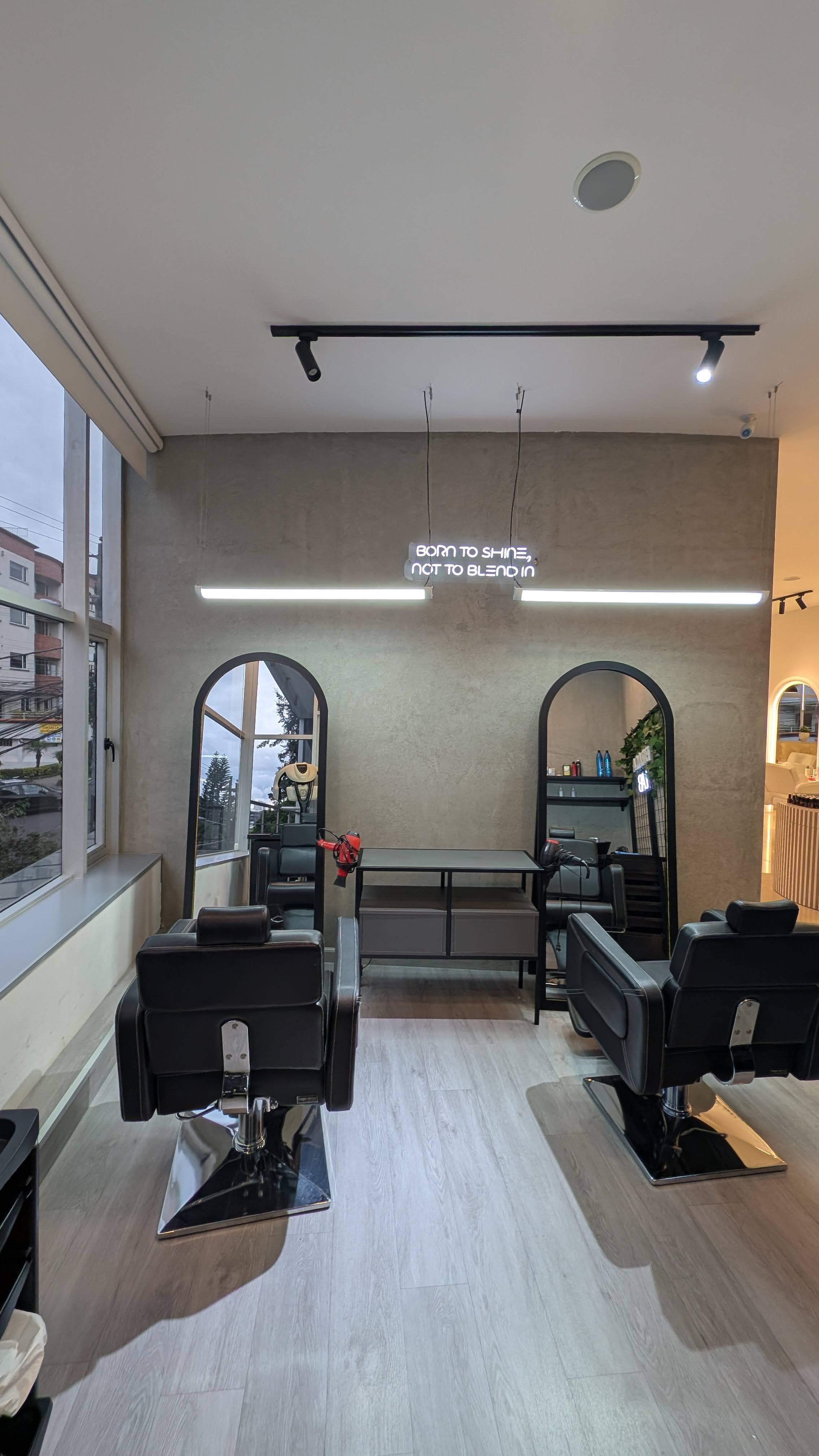 Area de estilismo con letrero neon Born to Shine Not to Blend In, espejos arqueados y sillones negros