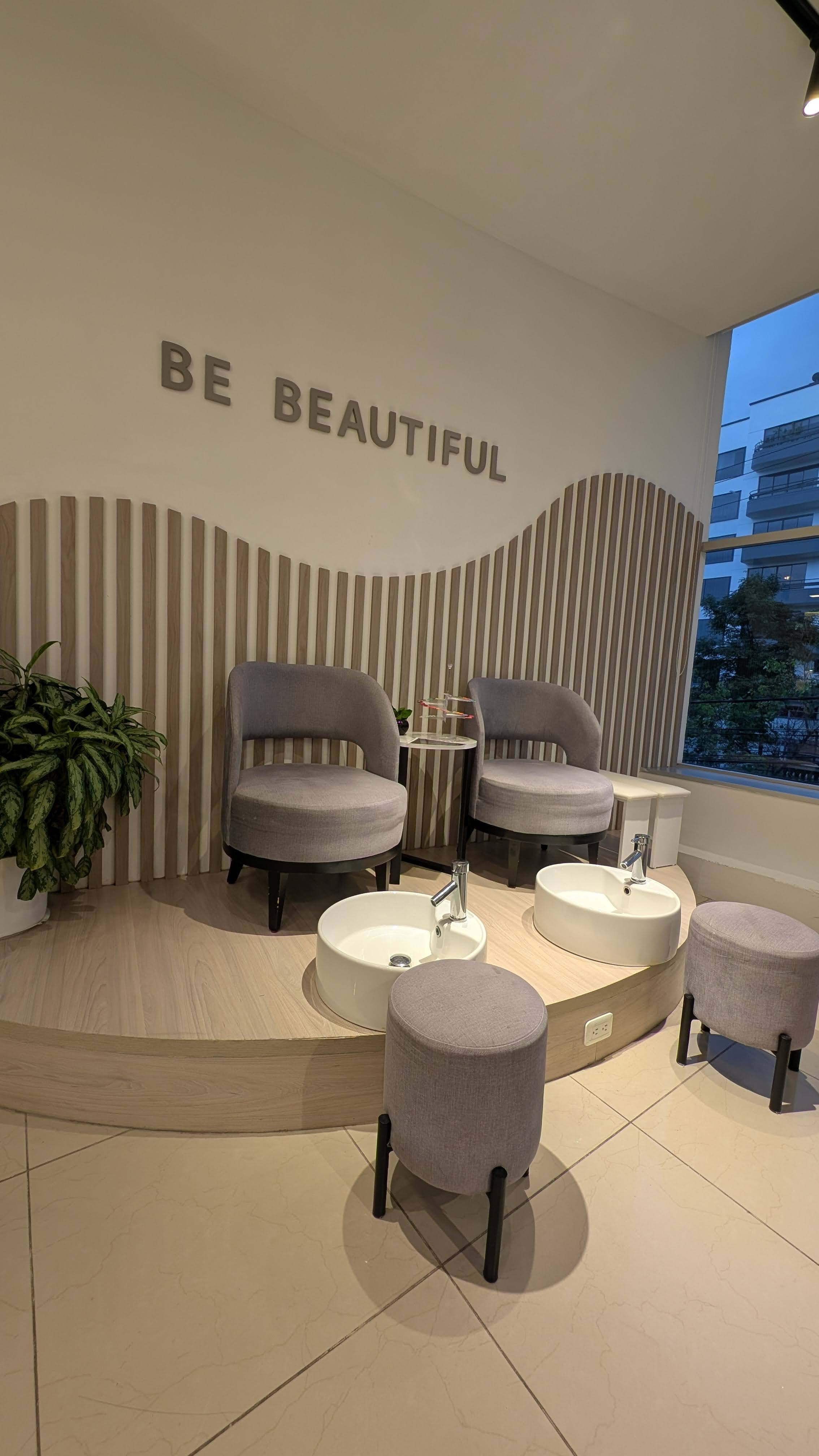 Area de pedicure con sillones de terciopelo gris, letrero Be Beautiful y decoracion de madera