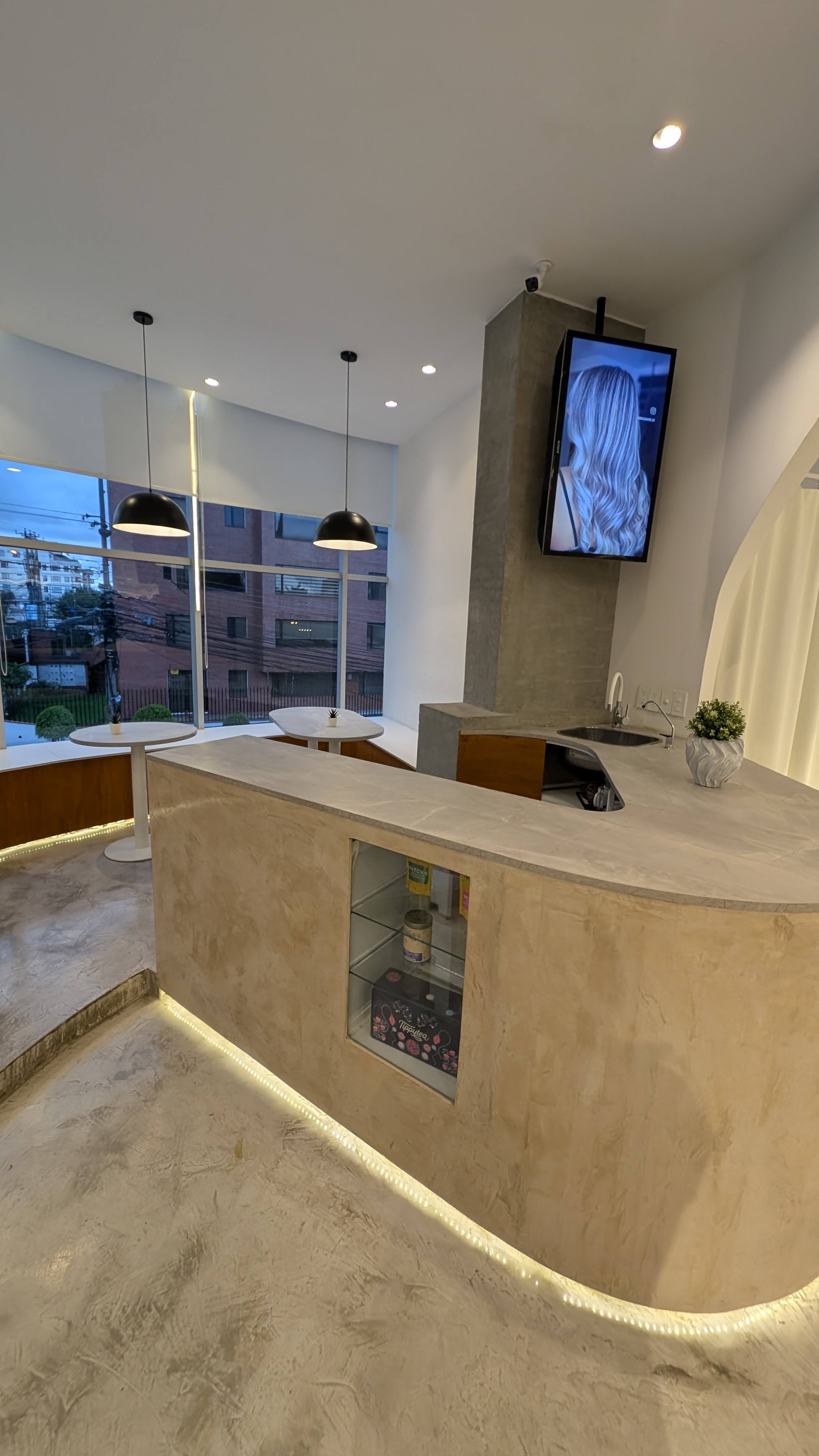 Recepcion BRACA Hair Lab con barra de concreto curva, lamparas colgantes y pantalla mostrando transformaciones